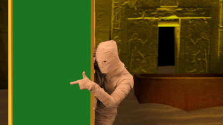 Egyptian pharaoh entombment. Scary a mummy peeking from behind a column with a green screen banner and pointing at it. Mock up, workspace for your promotion clip or advertisement.の写真素材