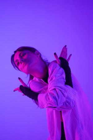 Young woman performing contemporary dance in studio. Neon pink and purple color scheme, ombre, gradient background. Medium sized.の写真素材