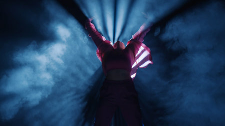 Silhouette of a woman dancing jazz-funk in a studio. Black background filled with smoke, white...