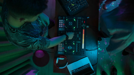 Top view shot capturing a man playing and mixing music on a DJ console for a crowd of people in...