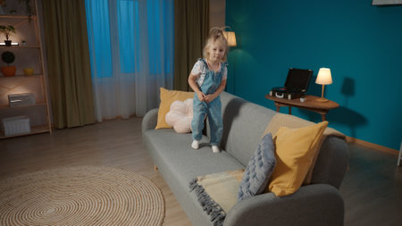 A little girl stands full length on the living room couch. Childrens games and entertainment at home. The concept of hyperactivity.の写真素材