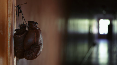 In the close up, shot, brown leather boxing gloves hang on a cord from a rusty nail on a door frame. In the background is an empty, dark corridor, someone has left their sport equipmentの写真素材