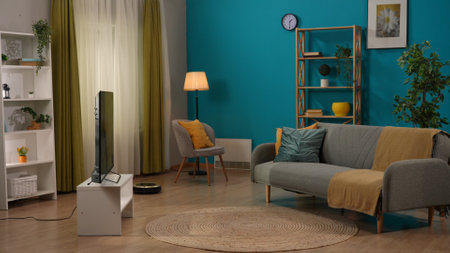 Home living room with sofa and TV screen, closets and chair, robot vacuum cleaner on the floor. Smart home concept.の写真素材