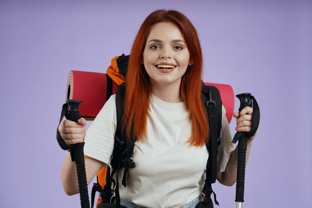 Woman tourist in casual with backpack holding trekking poles smiling at the camera. Isolated on purple background.の写真素材