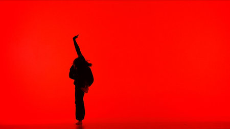 Attractive girl silhouette in black outfit holding hand up dancing element of contemporary dance on red background in studio.の写真素材