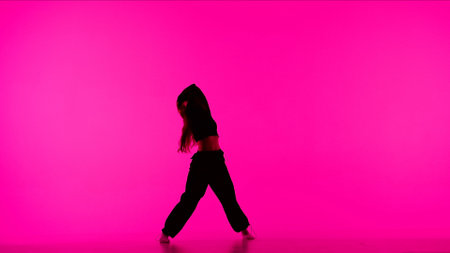 Attractive girl silhouette in black clothing showing dancing elements of contemporary dance on pink background in studio.の写真素材
