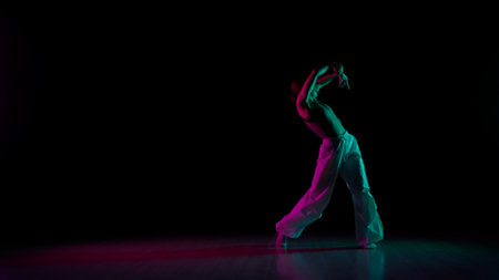 Attractive girl in casual posing at the camera, showing contemporary choreography, black background pink green neon light.の写真素材