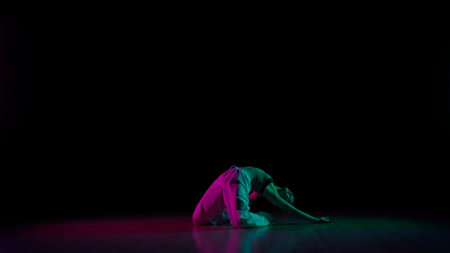 Attractive girl in casual posing on the floor, showing contemporary choreography, black background pink green neon light.の写真素材