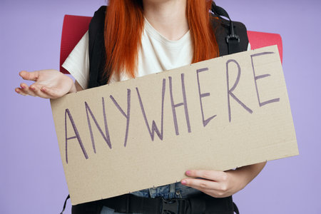 Woman tourist with backpack holding cardboard sign with word anywhere written on it, close up shot. Isolated on purple background.の写真素材