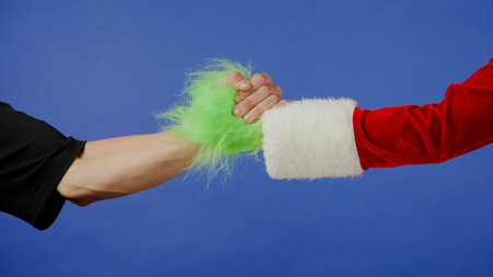 Greeting gestures of man and Grinchs hairy green hand on isolated blue background. Gift kidnapper cosplay. Christmas and New Year celebration concept. Blue screen, chroma key.の写真素材