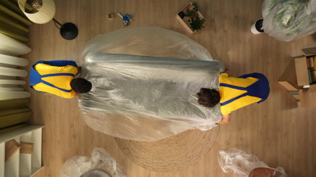 Top view of apartment living room. Delivery service male workers in uniform put sofa on the floor wrapped in film.の写真素材
