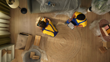 Top view of apartment living room. Delivery service male workers in uniform bring boxes with stuff and check them on list.の写真素材