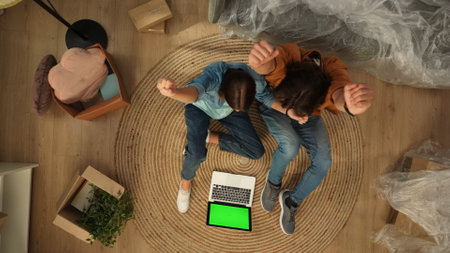 Top view of apartment living room. Man and woman sitting on the floor showing win gesture, laptop with chroma key green screen.の写真素材