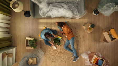 Top view of apartment living room. Man laying on the floor woman checking box with belongings in the room with packed furniture.の写真素材