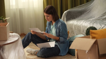 Close up shot of apartment living room. Woman sitting on the floor holding eviction documents,...