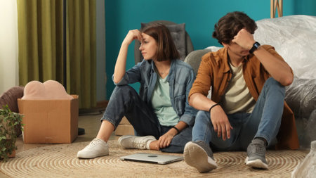 Close up shot of apartment living room. Man and woman sitting on the floor in the new apartment with laptop, upset expression.の写真素材
