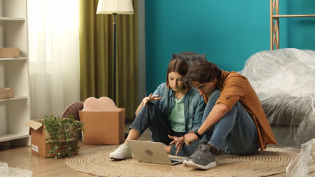 Close up shot of apartment living room. Man and woman sitting on the floor in the room and looking at laptop screen.の写真素材