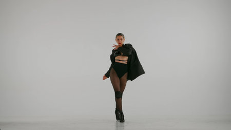 Framed on a white, gray background. Young woman, demonstrating dance moves towards high heels, squatting. She is wearing a beautiful red dress and . She is sexy, rhythmic, plastic. Medium shotの写真素材