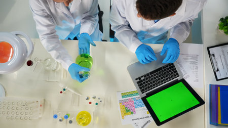 A close up of scientists sitting in the frame. A woman is holding a flask of liquid, she is looking...