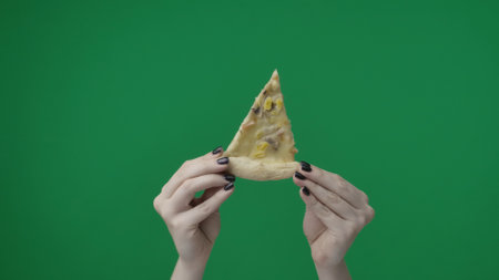 Close up shot on green chromakey background. A womans hand, she is holding a slice of pizza with toppings with her hands up. She demonstrates it to the camera, shows it, shares itの写真素材