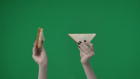 In the close up shot on the green background. The female hand holds two breadcrumbs with a...