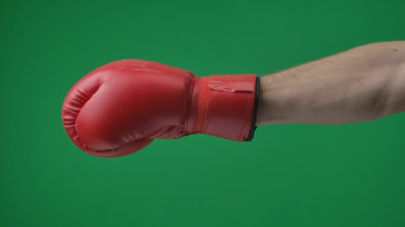 In the shot close up on a green background, chromed. Man in a red, leather boxing glove. He stretches out his hand, shows a blow, training. You can only see the hand. Medium frameの写真素材
