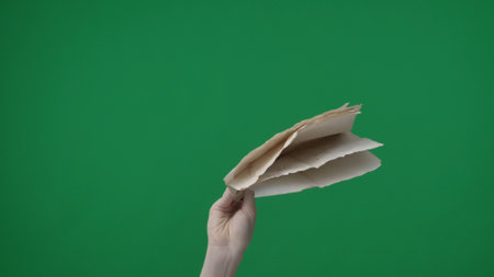 Framed on a green background, chromakey. A womans hand with a manicure holds a small stack of crumpled white sheets of paper. She holds them above her with her side facing the camera.の写真素材
