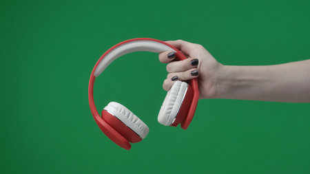 In the frame on a green background, a lame key female hand with a manicure holds and extends red wireless headphones for listening to music. Here can be your advertising. Medium frameの写真素材