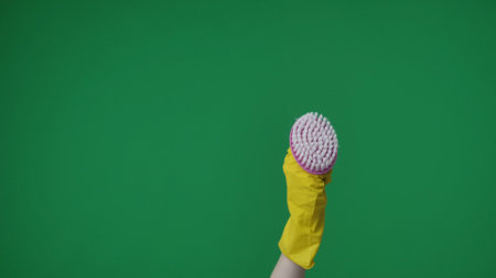 In the frame on a green background, a lame female hand in a yellow rubber glove holds and demonstrates a brush. Used for cleaning and cleaning items. Here can be your advertising. Medium frameの写真素材