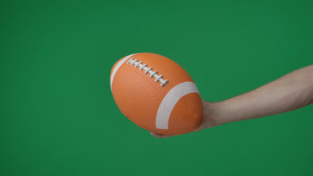 In a shot on a green background, chromakey male hand that holds, holds out an oval shaped ball for American soccer, it is inflated, bright color. This could be a place for your advertisement.の写真素材