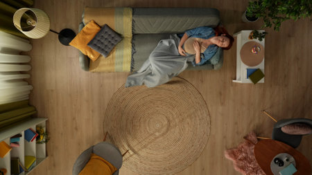 In the shot above, a pregnant woman in a room is lying on a sofa covered with a plaid. She is...