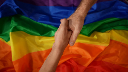Top view detail shot capturing two male hands reaching for a handshake from the opposite corners of the frame. LGBT flag on the background.の写真素材