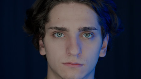 Portrait of a young man illuminated in blue color from a monitor screen on a black background close...
