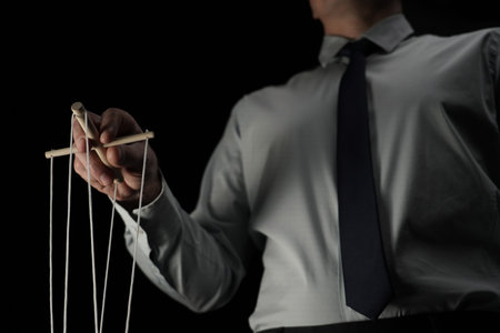 In the frame against a black background stands a man in a suit holding a device with ropes that hold a puppet. Depicts a businessman who manages someone, directs. Theatrical performanceの写真素材