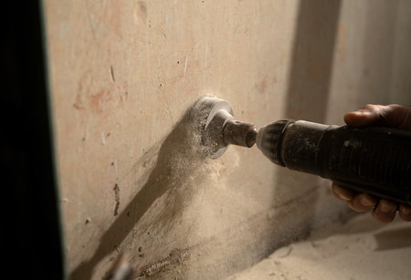 In the frame, the man is doing repairs in a room filled with dust. He drills a concrete wall with a hole, cuts something on the wall. The dust is flying in different directionsの写真素材