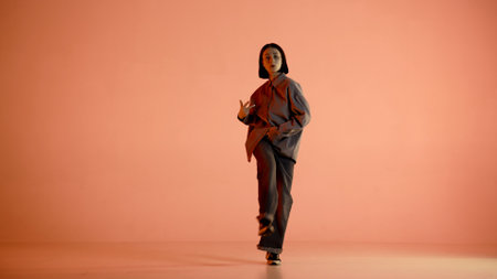 In the picture on an orange, light background. Dances young, beautiful girl. Demonstrates dance moves in the style of hip hop. She looks at the camera. Shes wearing comfortable clothes. The rhythmicの写真素材