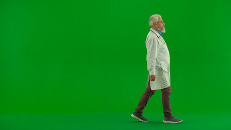 Portrait of man medic in studio on chroma key green screen. Senior doctor in white uniform walking looking at the side confident expression. Close up shot.の写真素材