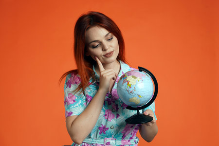 Close up of woman holding globe, thinking looking at the map and choosing best destination, isolated on orange background. Portrait of female traveler.の写真素材