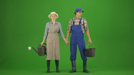Portrait of farmer in working clothing on chroma key green screen. Gardener man and woman with watering can and bucket holding hands.の写真素材