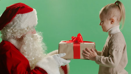 Santa claus giving Christmas gifts box with red ribbon to child on green background.の写真素材