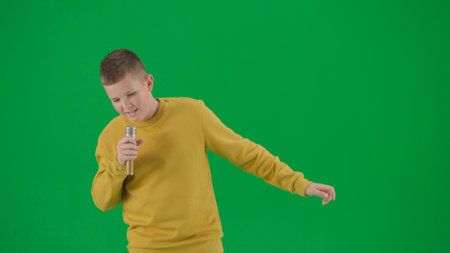 Portrait of kid boy on chroma key green screen. Schoolboy in jeans holding holding karaoke microphone and singing song. Middle body front shot.の写真素材