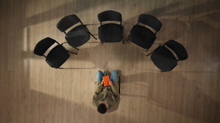 In the frame above, a middle aged man is sitting on a chair in the center. He is waiting for his group meeting to start, thinking about something, thinking. He is holding an orange notebook. Top viewの写真素材