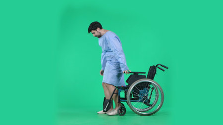 Adult man patient in robe standing from wheelchair ready to make few steps without support, focused expression. Isolated on chroma key green screen.の写真素材