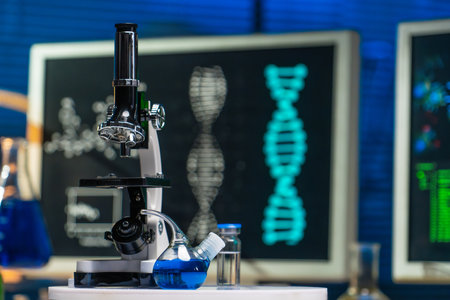 In the close up shot, the laboratory room is shown. On the table there is a microscope, test tubes and flask with blue liquid. The computer monitors show spirals of DNA.の写真素材
