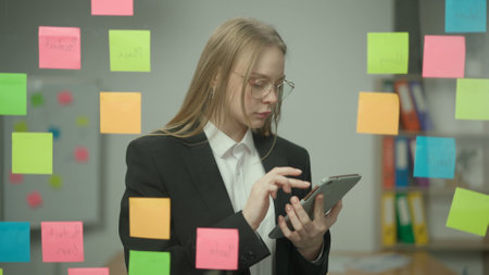 Portrait of corporate leader in office planning project on notes. Business woman holding tablet and looking at sticky notes on glass wall.の写真素材