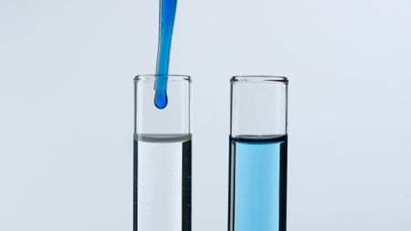 Two glass test tubes on a white background. Test tubes are filled with liquid, a blue substance is dripping into one of them from a pipette. Concept of medicine, biochemical research. Close-up.の写真素材