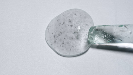 Close up shot of transparent substance on the white background. Glass pipette pouring cosmetic...