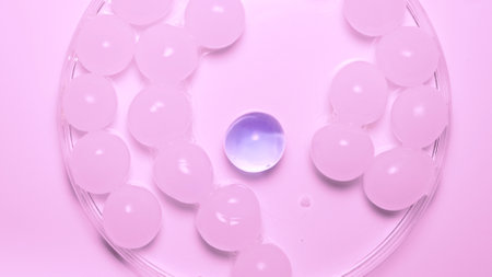 Lots of white hydrogel spheres with one purple one in pink light The shiny round spheres of gel...