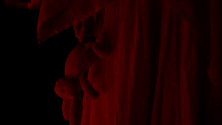 Horror movie and poltergeist creative advertising concept. Female ghost in a house. A woman in a white dress is walking down a hallway holding a toy. Red horror light. Close up.の写真素材