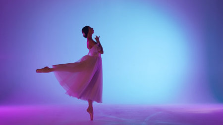 Portrait of female on purple background in pink neon light studio. Gentle ballerina in white tulle dancing jumping element of choreography.の写真素材